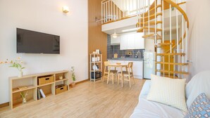 Uma sala de estar moderna com televisão de tela plana, piso de madeira, área de jantar com mesa e cadeiras, escada e cozinha.