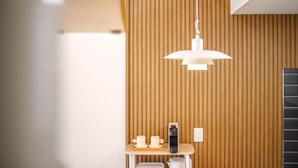Um interior moderno com painel de parede em madeira, luminária pendente, uma pequena mesa com xícaras e um telefone, e uma lixeira.