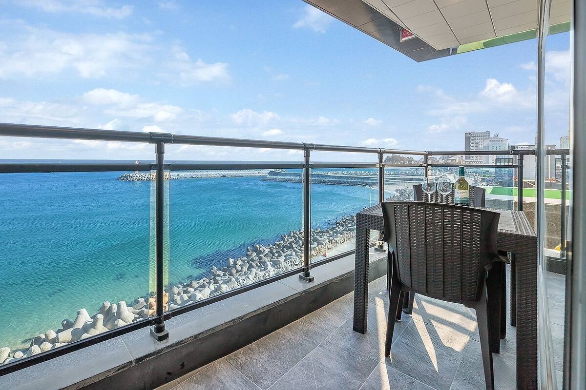 Un balcón con vista al mar, una silla y una mesa con una botella.