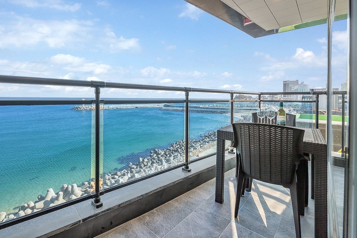 Un balcon avec vue sur la mer, une chaise et une table avec une bouteille.