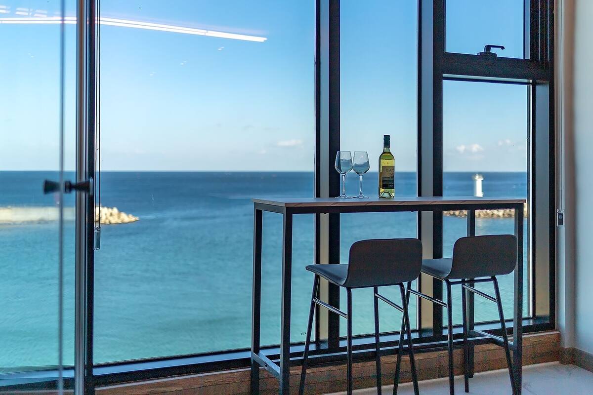Una habitación con vista al mar, una mesa con dos sillas y una botella de vino.