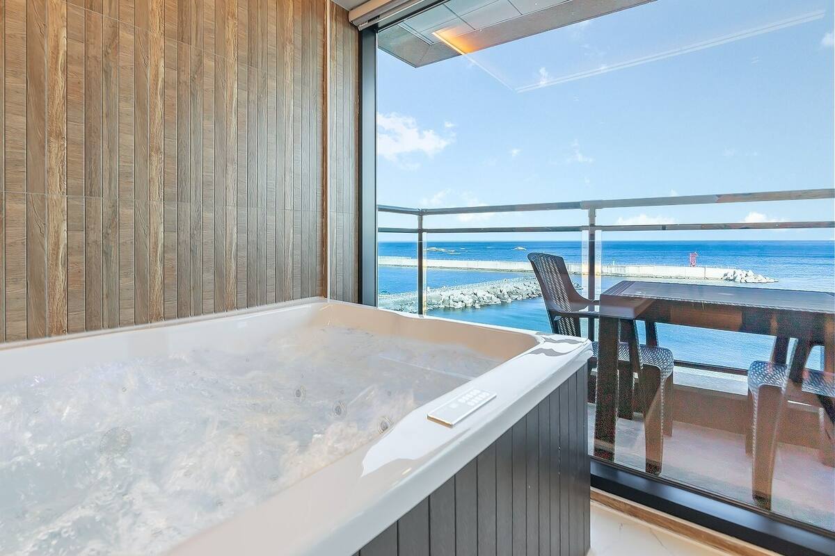Una habitación con una bañera grande, paneles de madera en las paredes y vistas al océano.