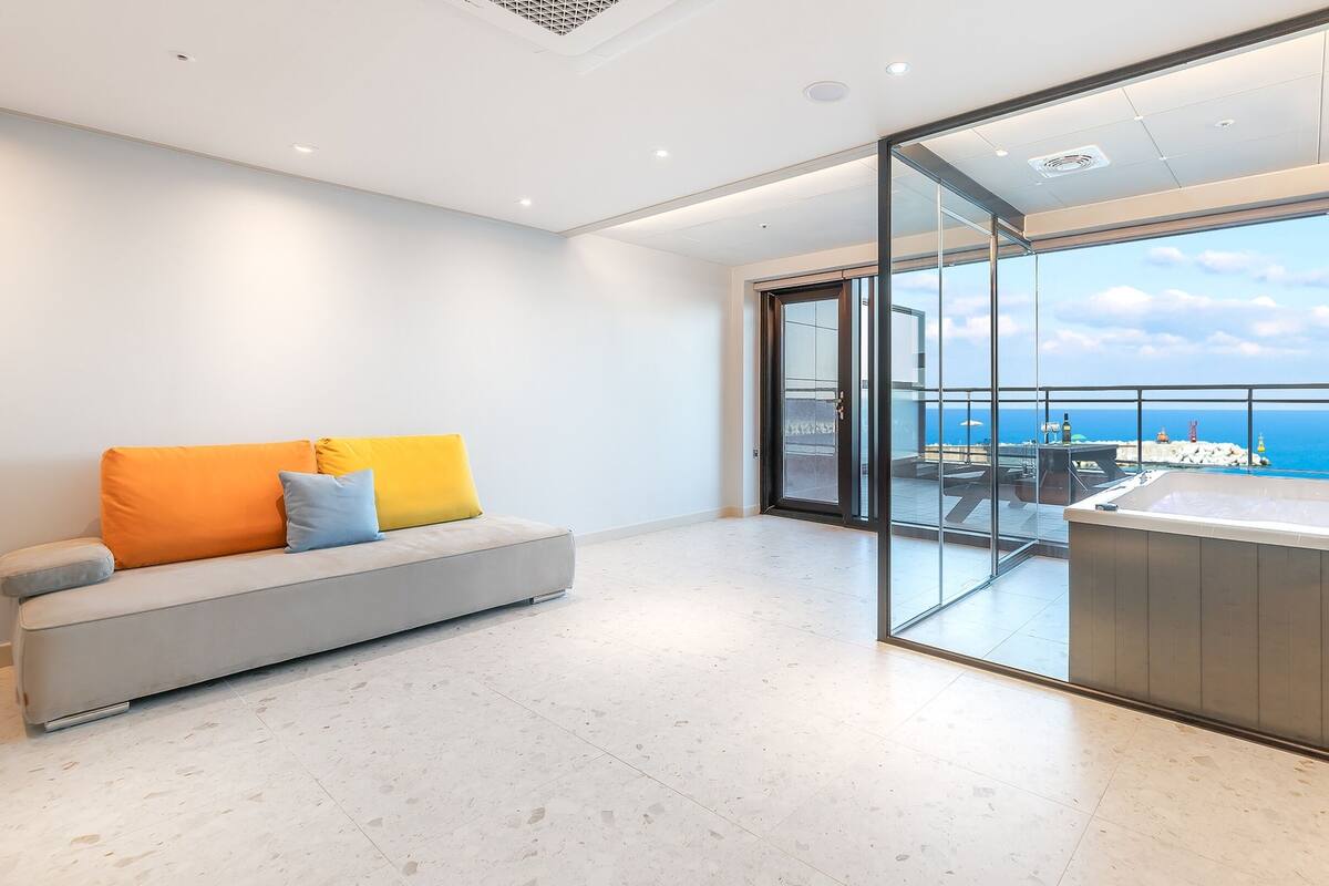 Un espacio moderno para estar con un sofá, un separador de vidrio y vista al mar.
