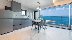 A modern kitchen with a large window overlooking the sea, a dining area with a table and chairs, and a balcony with a view of the ocean.