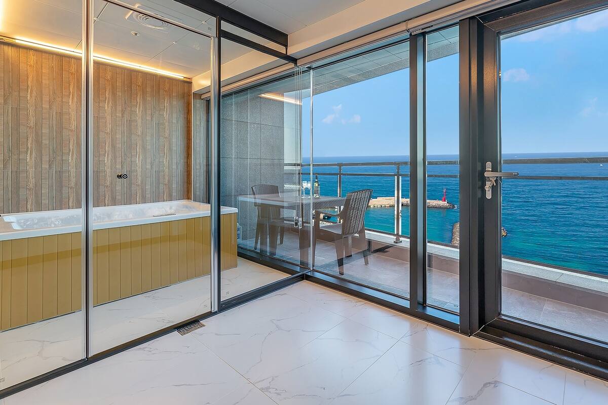 Un baño moderno con mampara de vidrio, tocador de madera y vista al océano.