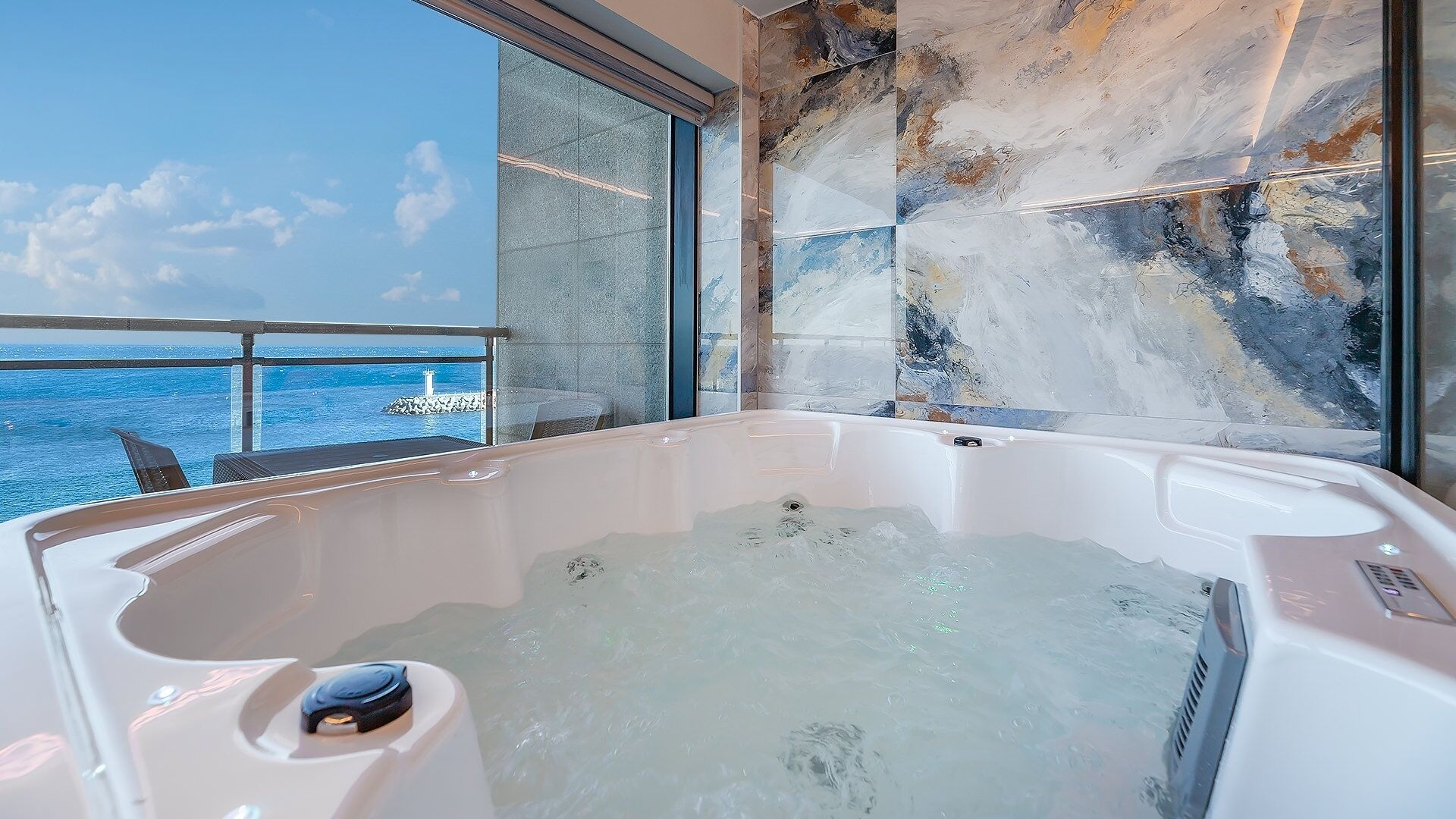 A hot tub with a view of the ocean and a stone wall.