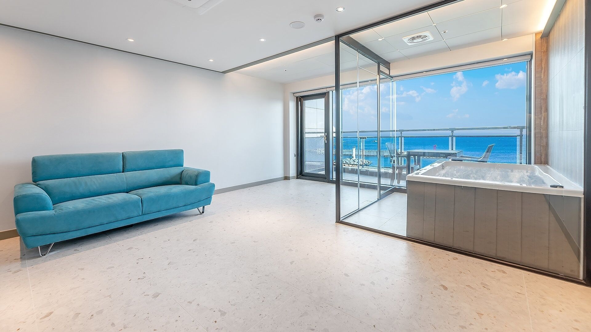 A modern room with a blue sofa, a glass wall, and a view of the sea.