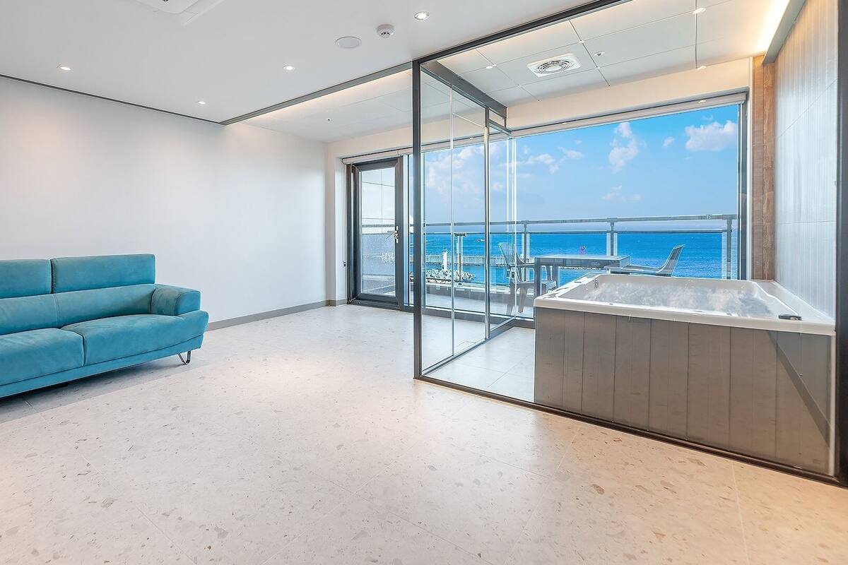 Una habitación moderna con un sofá azul, un muro de cristal y vistas al mar.
