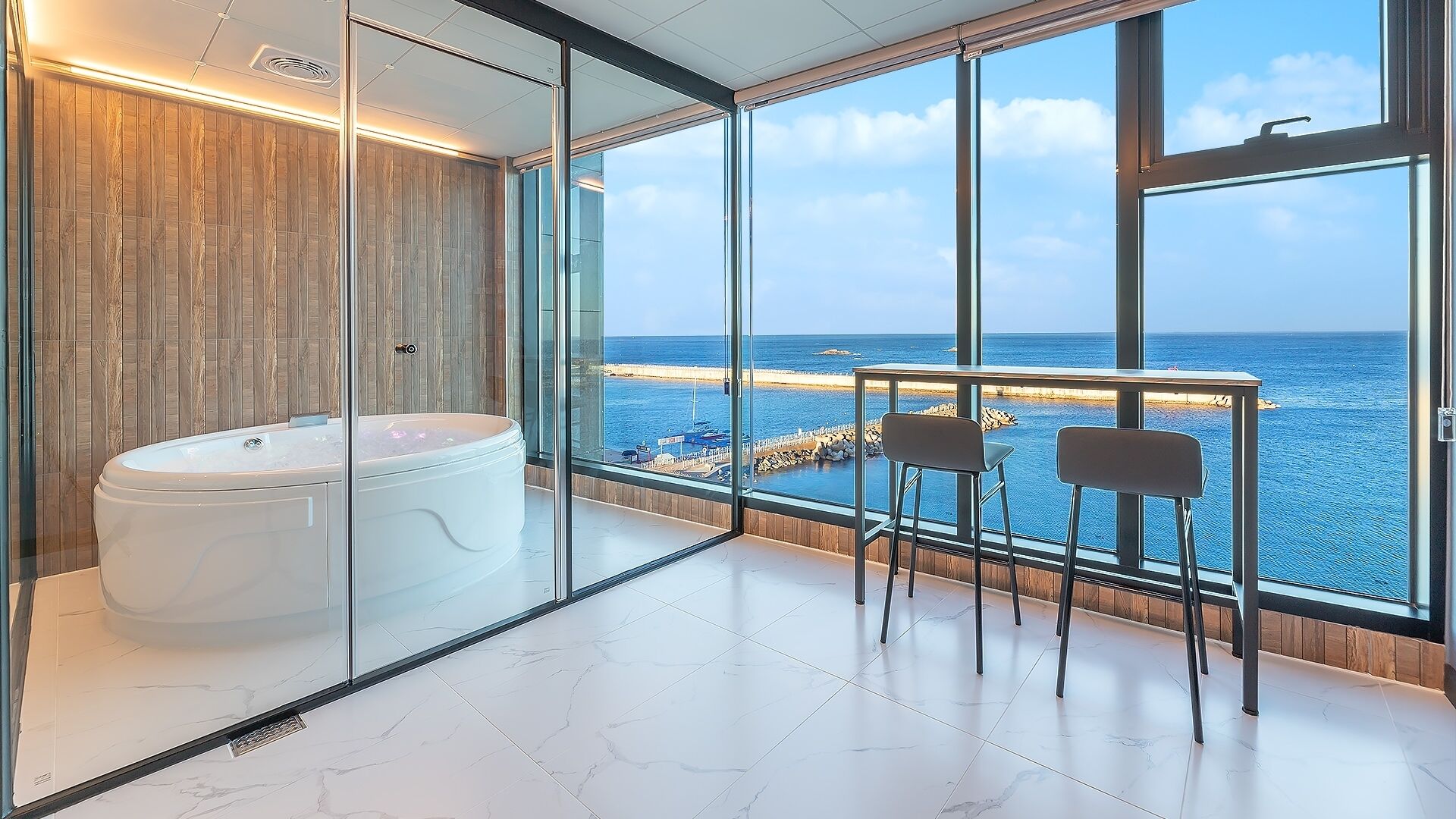 A modern bathroom with a jacuzzi, a glass partition, and a view of the sea.