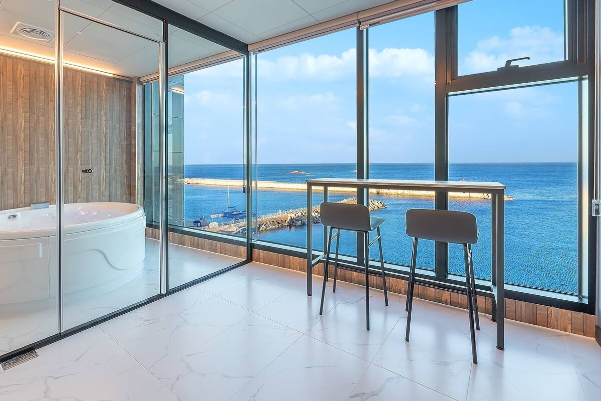 Un baño moderno con jacuzzi, mampara de vidrio y vistas al mar.