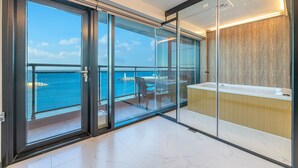 A modern balcony with glass doors, a view of the sea, and a small seating area with a table and chairs.