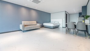 A modern bedroom with a bed, a sofa, and a dining area with chairs. - Sokcho The Sharp Pension (Sokcho)