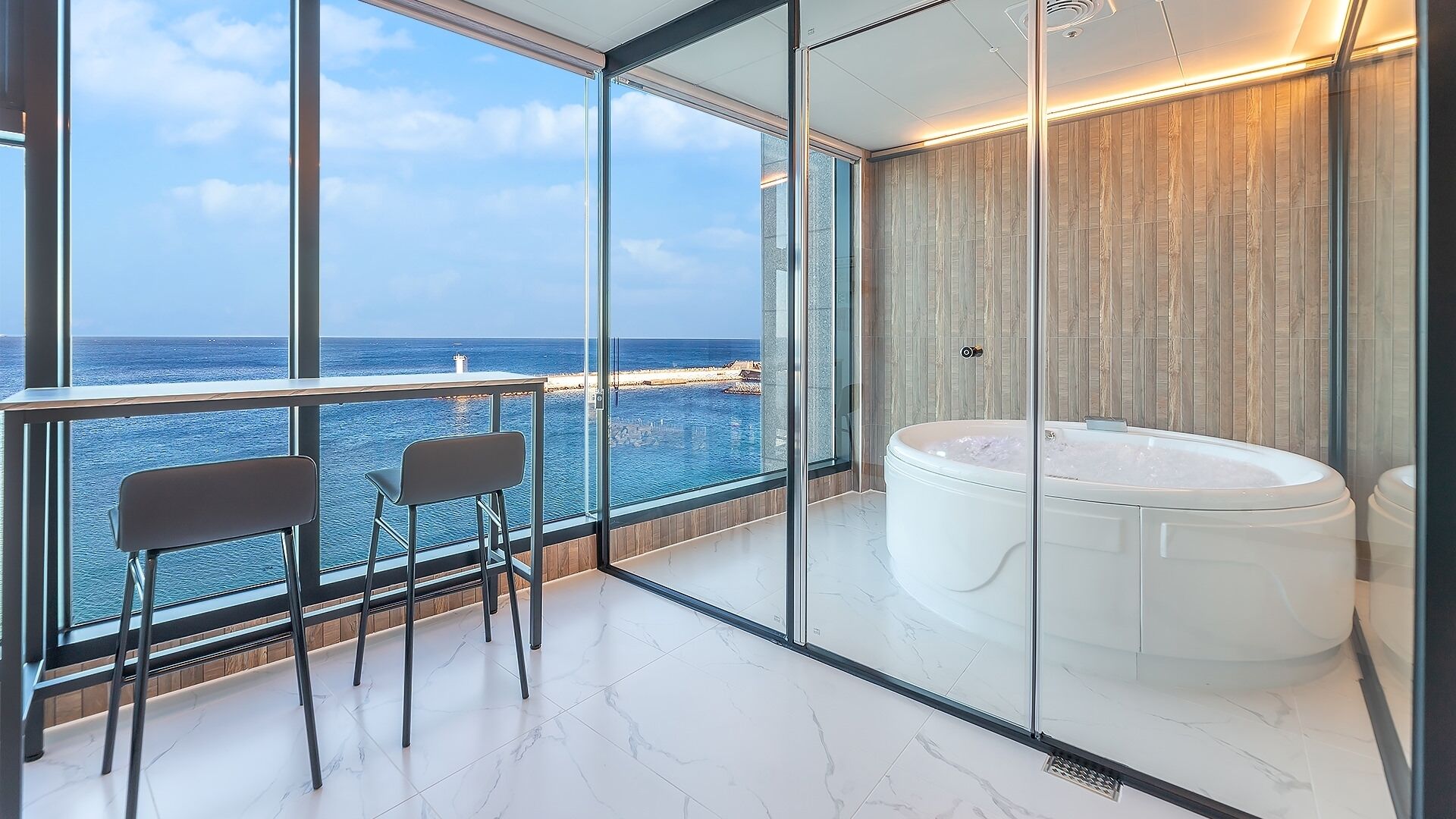 A balcony with a view of the sea, a jacuzzi, and a seating area with chairs.