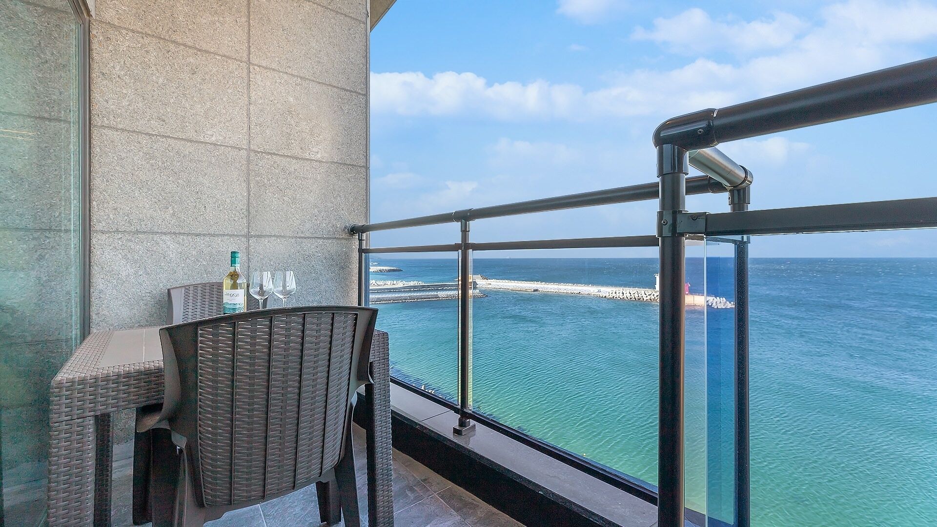 A balcony with a wicker chair, a table, and a bottle of wine.