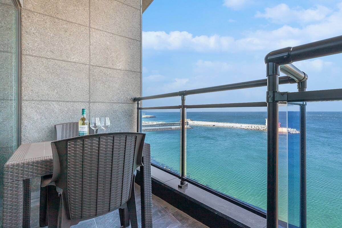 Un balcón con una silla de mimbre, una mesa y una botella de vino.