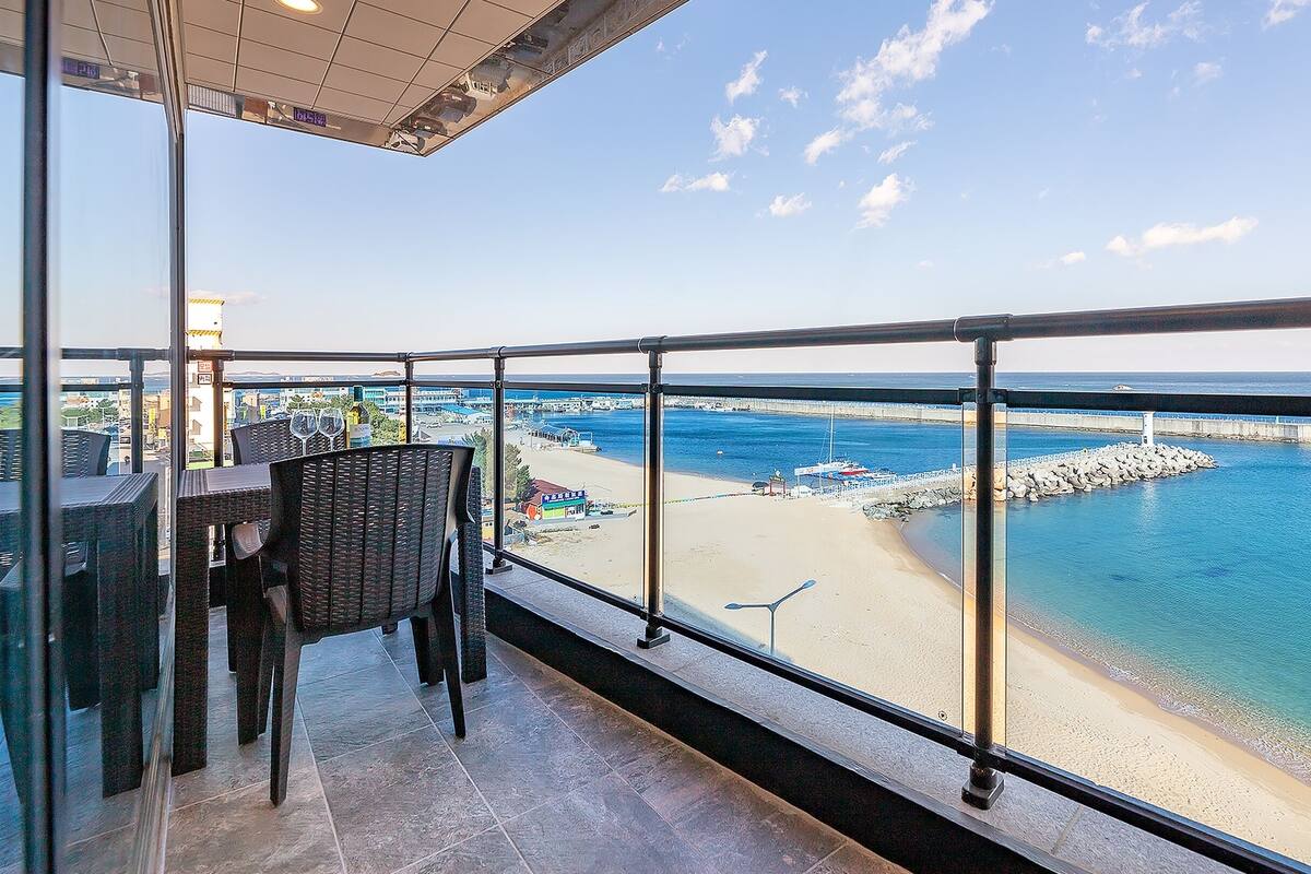 Balcón con mobiliario de mimbre que da a una playa y un muelle.