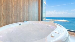 A spa room with a large hot tub, wooden panel walls, and a view of the sea.