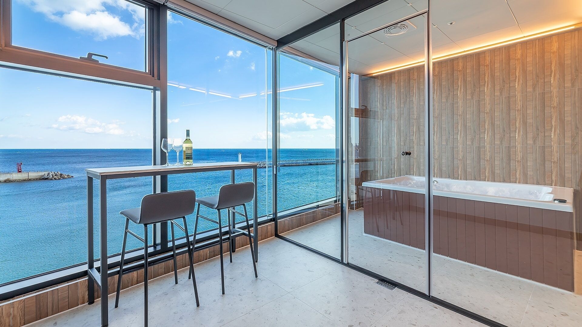 A balcony with a view of the sea, a glass partition, and a bathtub.