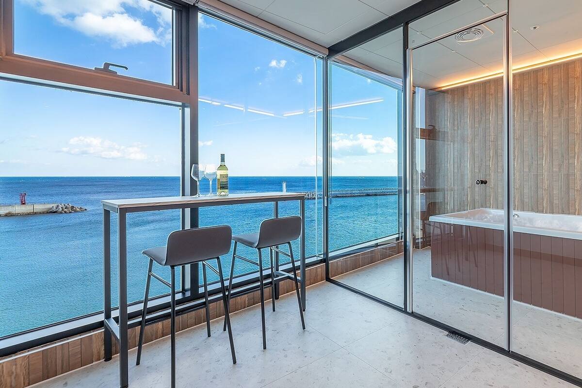 Un balcón con vista al mar, una mampara de vidrio y una bañera.