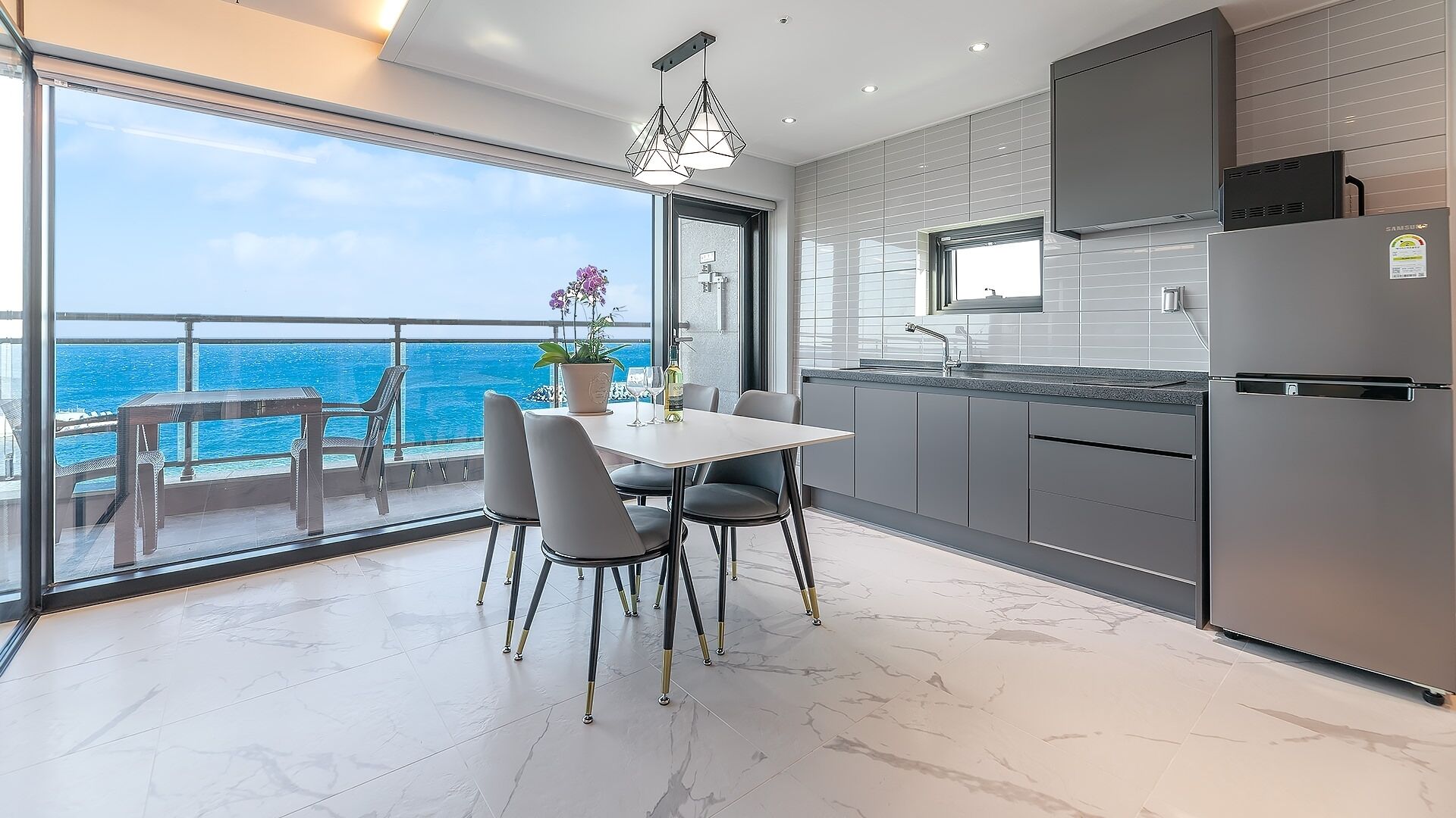 A modern kitchen with a view of the ocean, a dining area with chairs, and a large window.