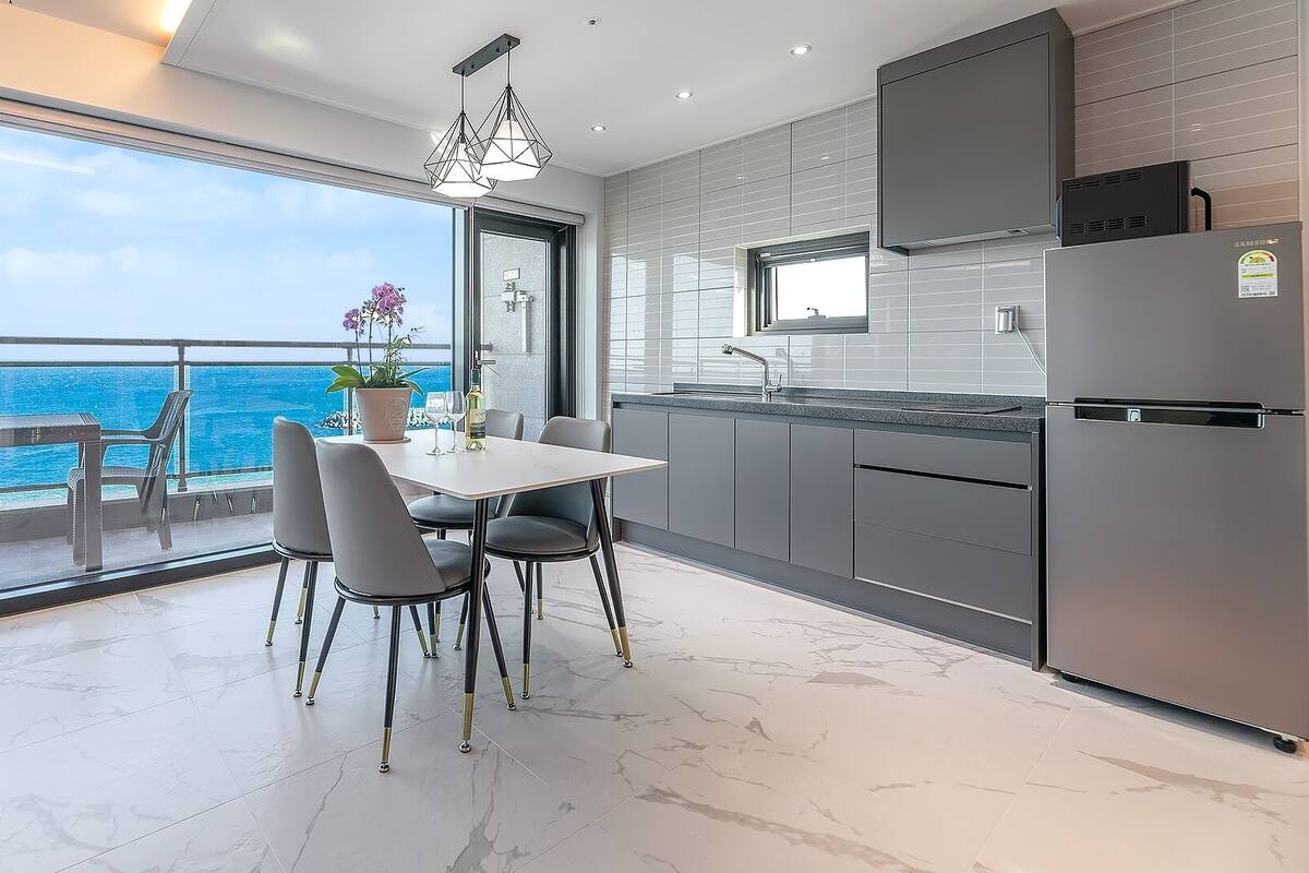 Una cocina moderna con vistas al océano, un comedor con sillas y un ventanal grande.