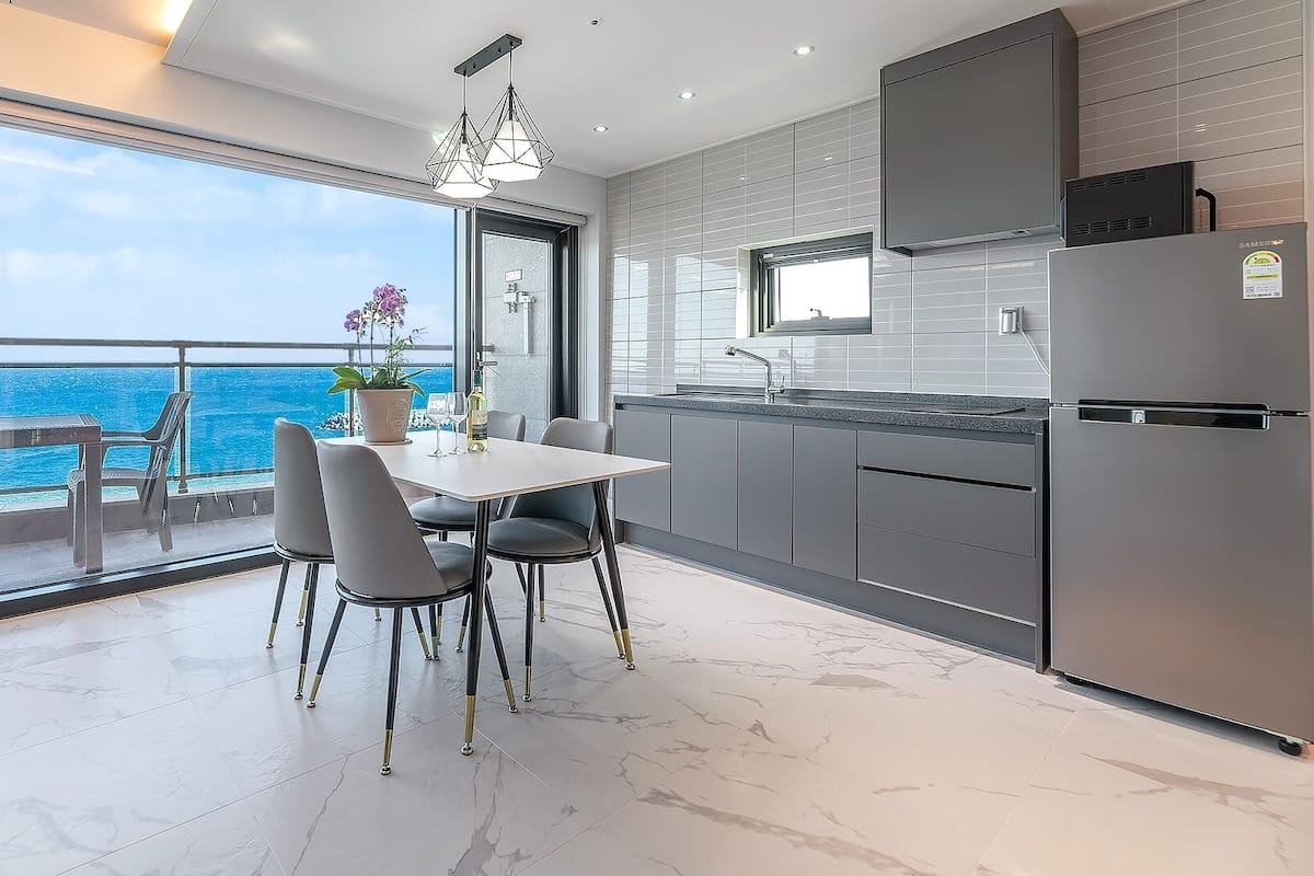 Une cuisine moderne avec vue sur l’océan, un coin repas avec des chaises et une grande fenêtre.