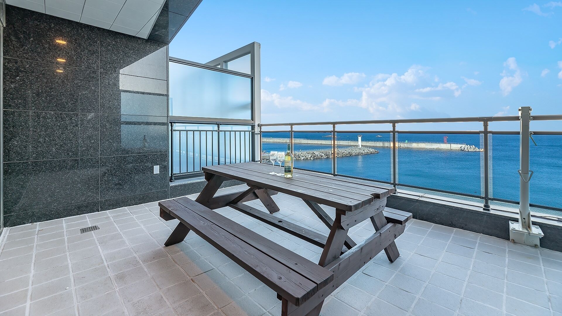 A balcony with a wooden table and chairs, a bottle of wine, and a view of the sea.