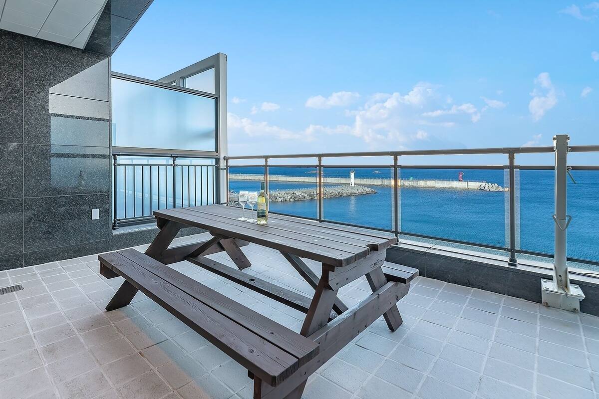 Un balcón con una mesa y sillas de madera, una botella de vino y vistas al mar.