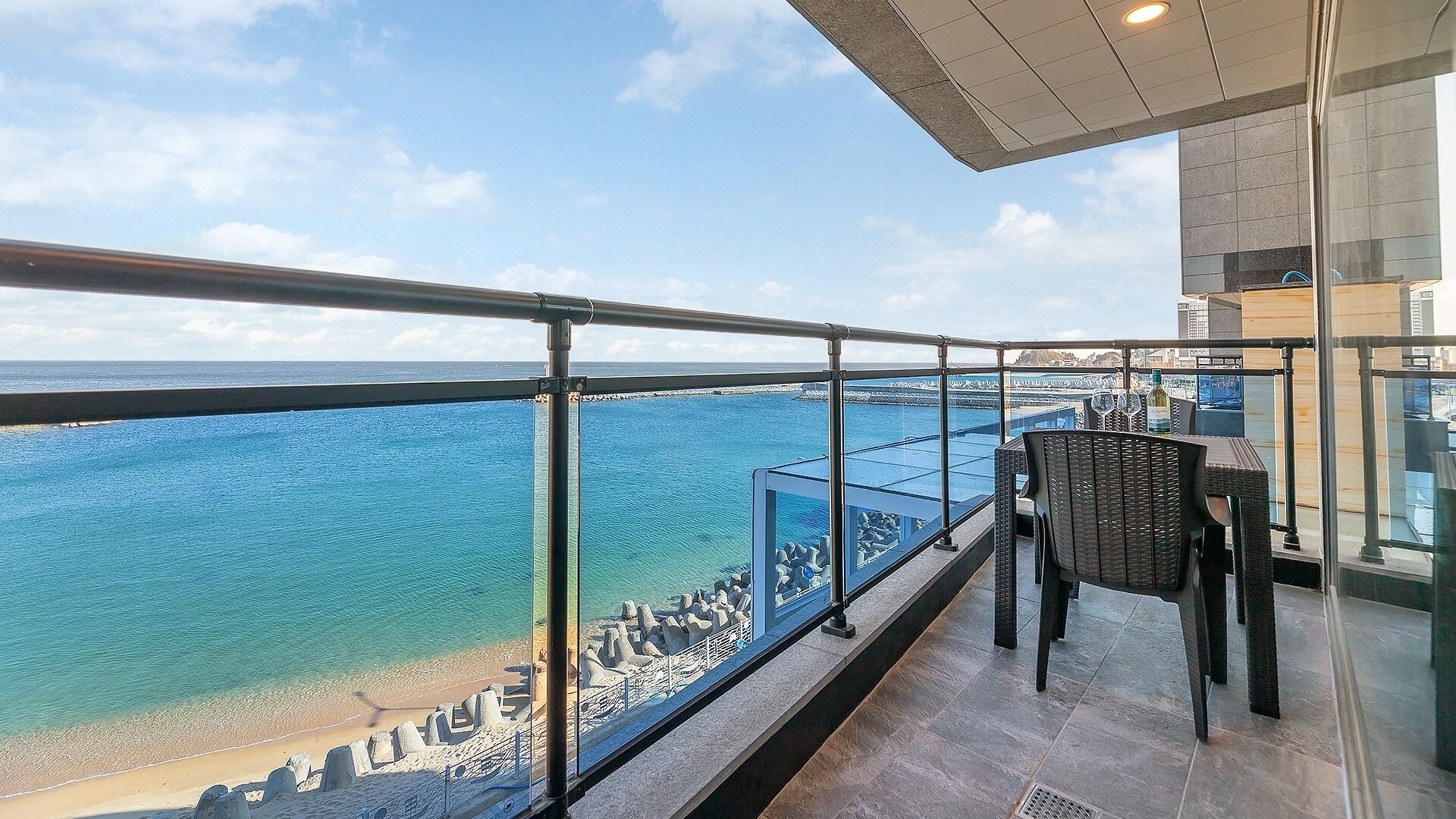 A balcony with a view of the sea, a glass railing, and a table with chairs.