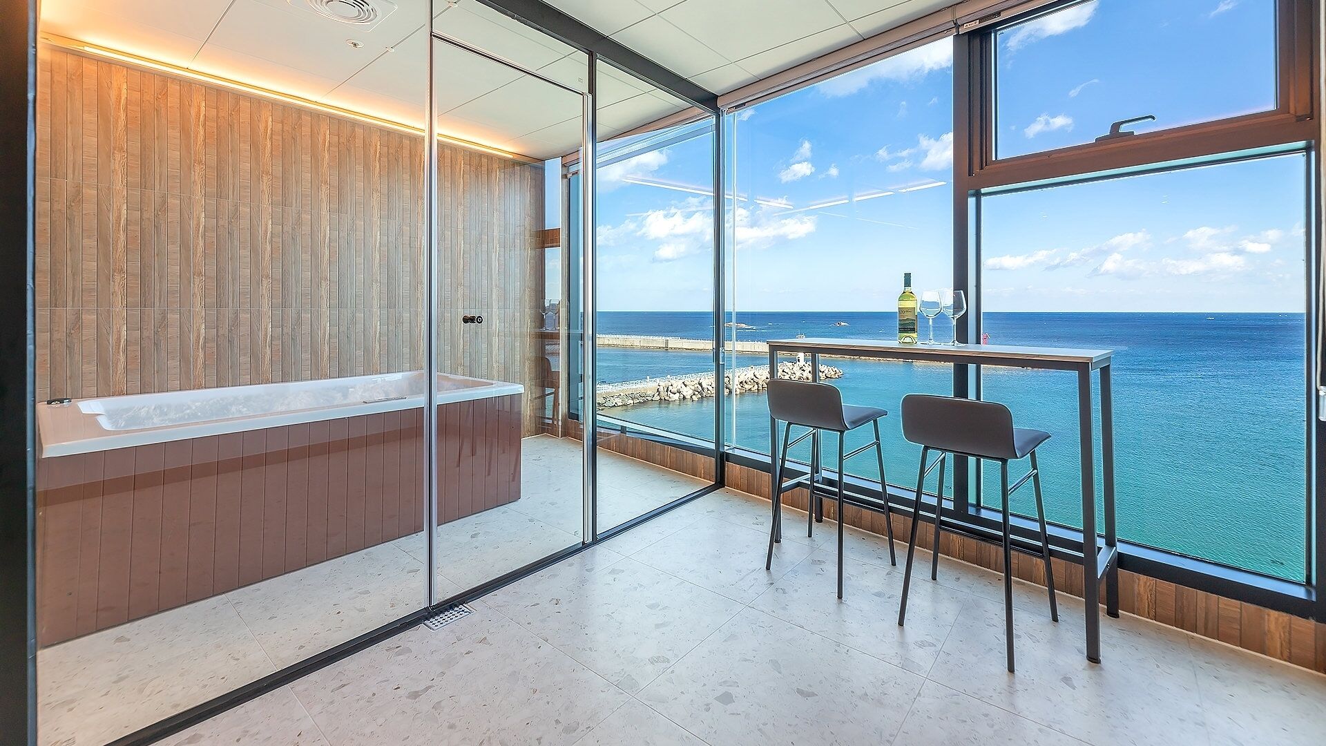 A modern bathroom with a glass partition, a wooden vanity, and a large window overlooking the sea.