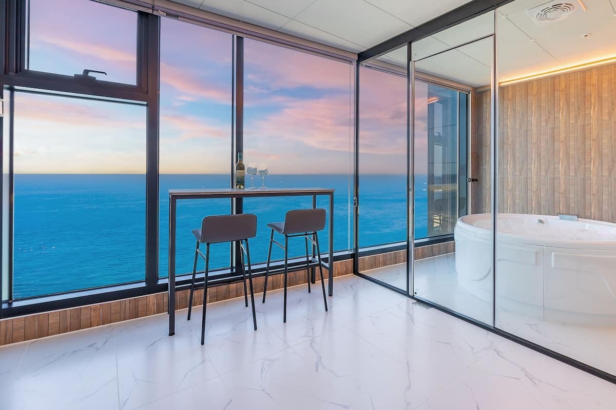 Una habitación moderna con vista panorámica al océano, un jacuzzi con paredes de vidrio y una zona de estar minimalista.