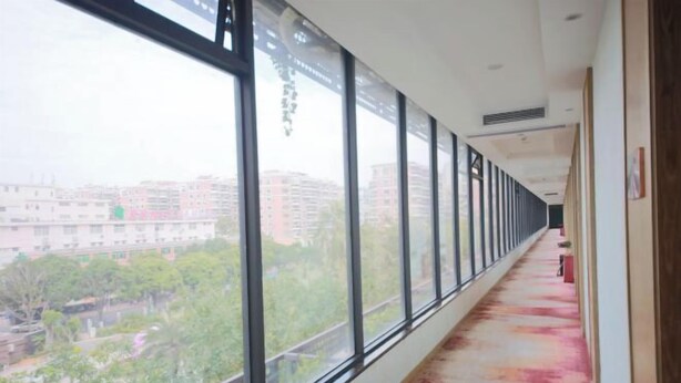 A corridor with large windows, a red carpet, and a view of buildings and greenery outside. - Great Wall Hotel (Xiamen)