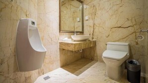 A bathroom with a marble wall, a sink, a toilet, a mirror, and a hand dryer. - Great Wall Hotel (Xiamen)