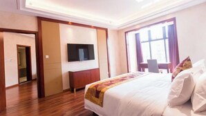 A hotel room with a large bed, a flat-screen TV mounted on the wall, a wooden wardrobe, and a window with curtains. - Great Wall Hotel (Xiamen)