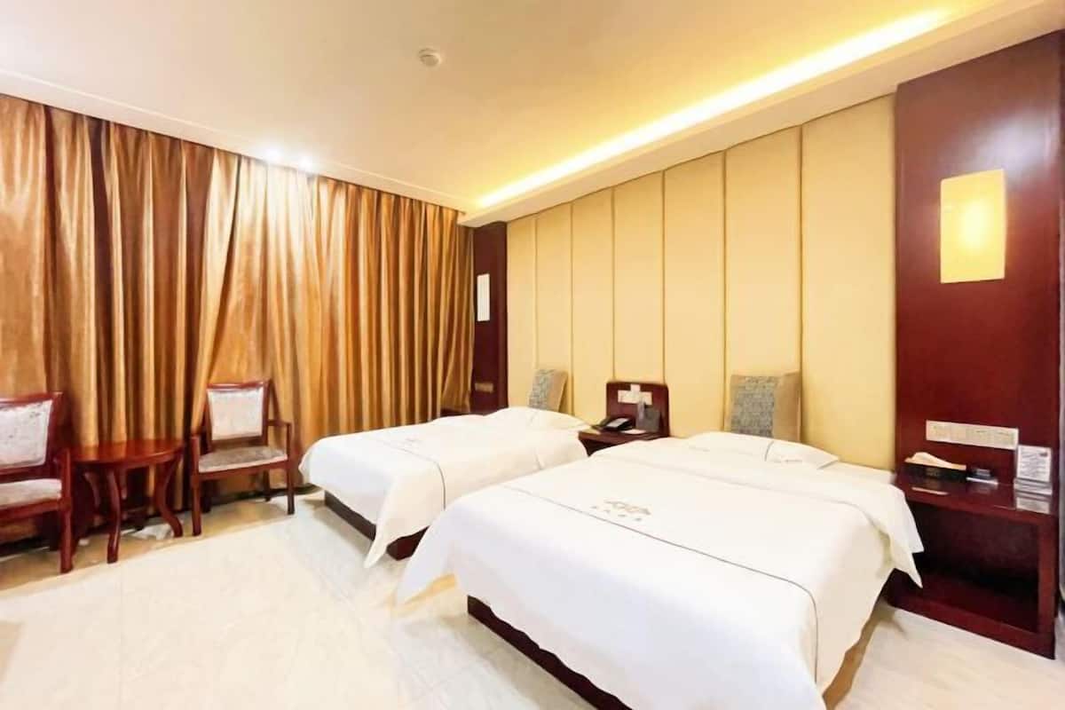 A hotel room with two beds, a desk, a chair, and a large window with curtains.