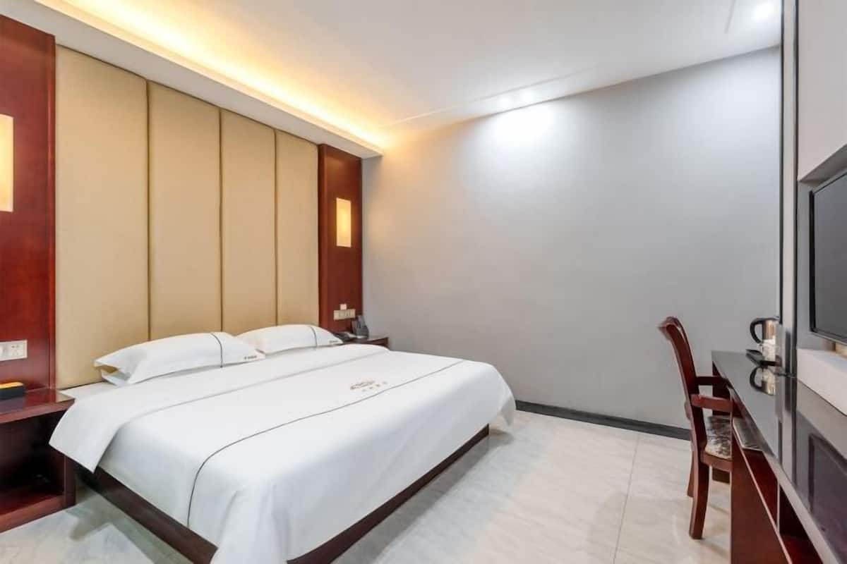 A hotel room with a bed, bedside tables, a desk with a chair, and a television.