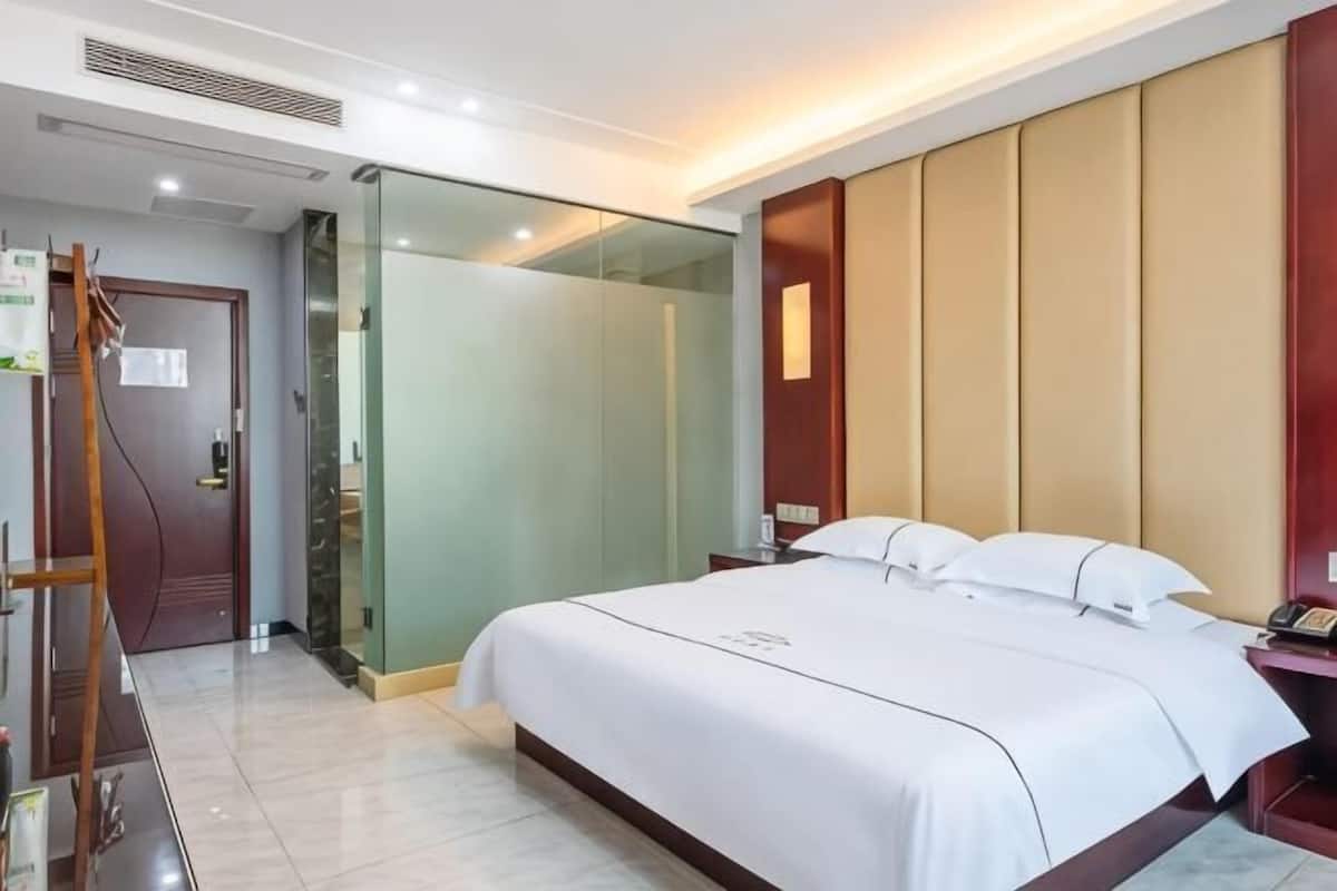 A hotel room with a bed, a desk, a chair, a wardrobe, and a glass partition.