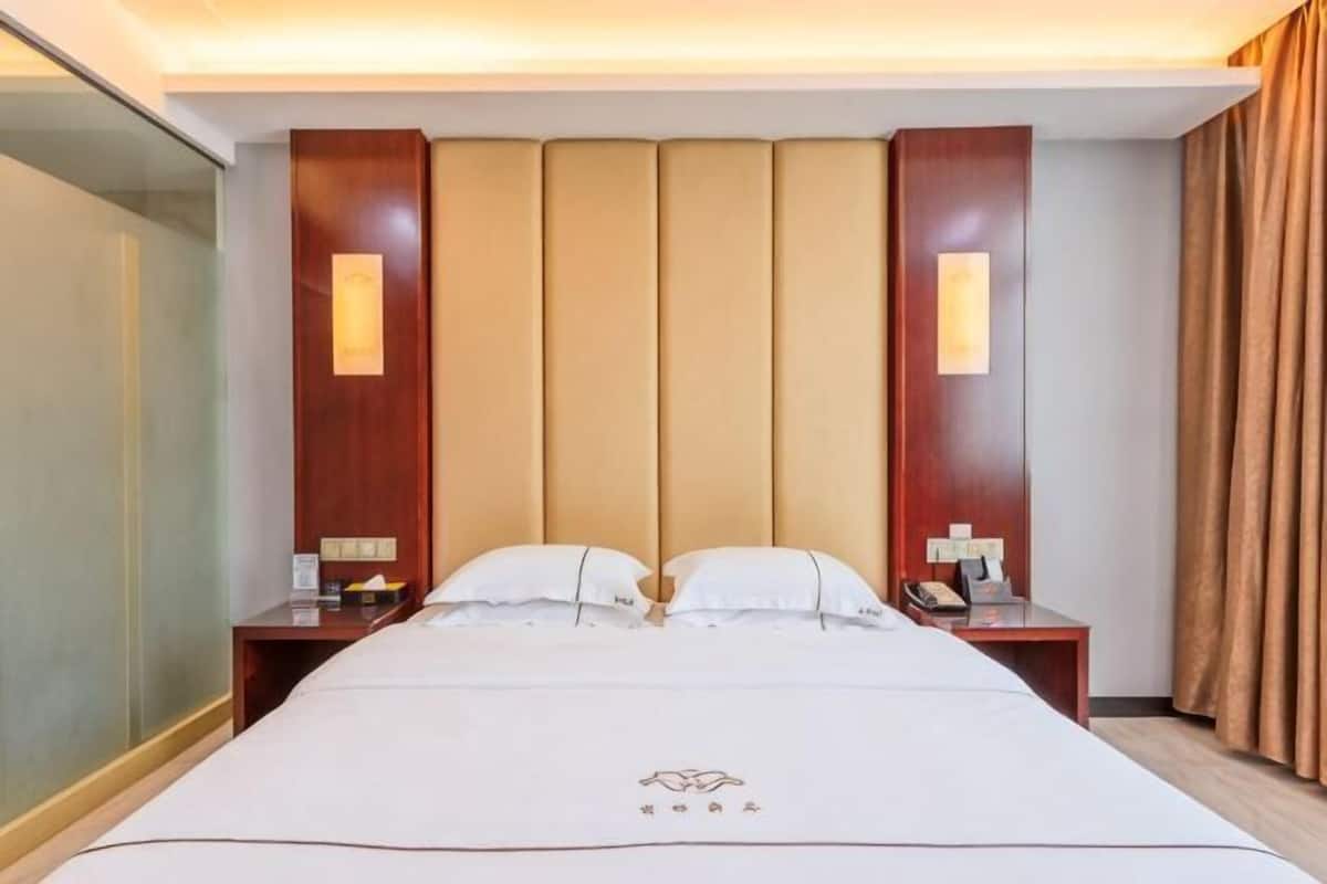 A hotel room with a large bed, two bedside tables, a headboard with vertical panels, and a curtain on the right side.