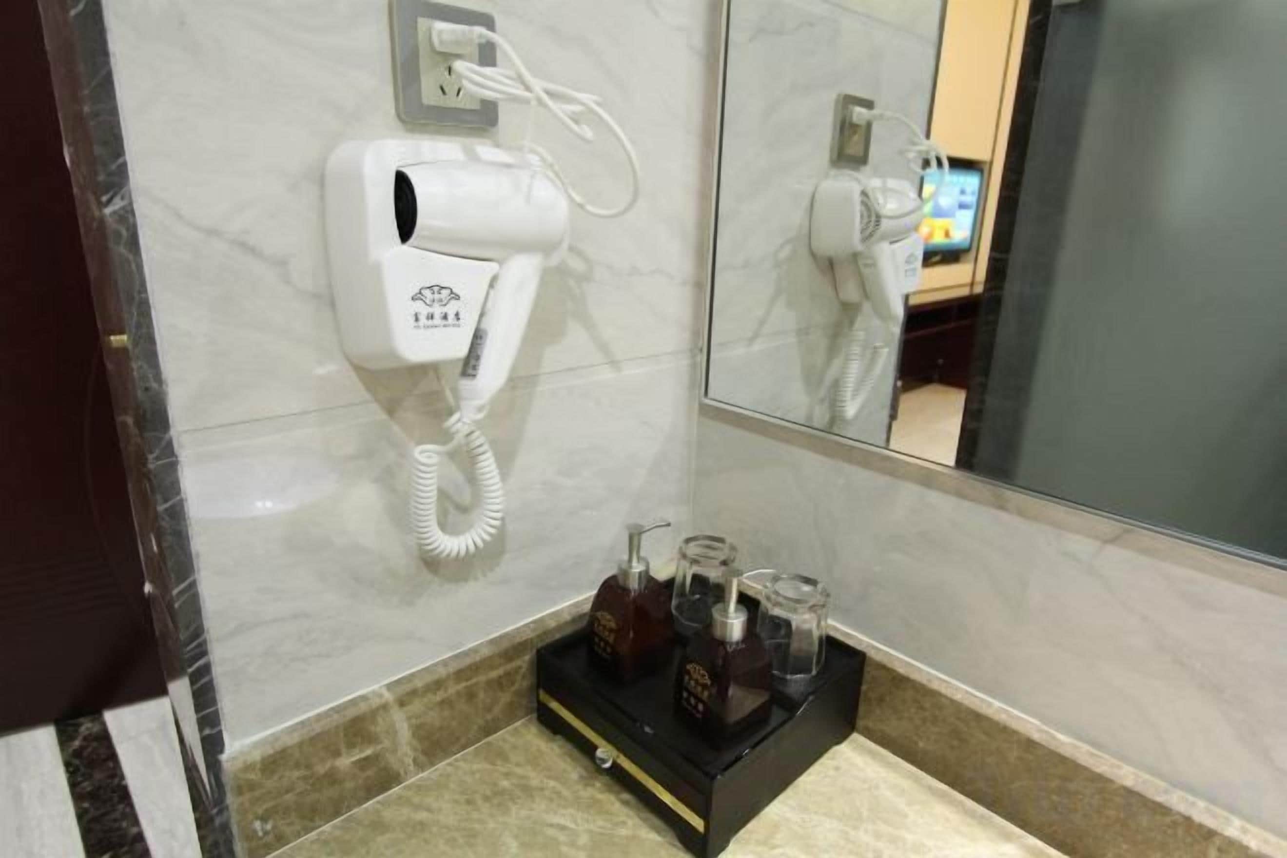 Casa de banho de hotel com secador de cabelo fixado na parede, espelho e bandeja com artigos de higiene.