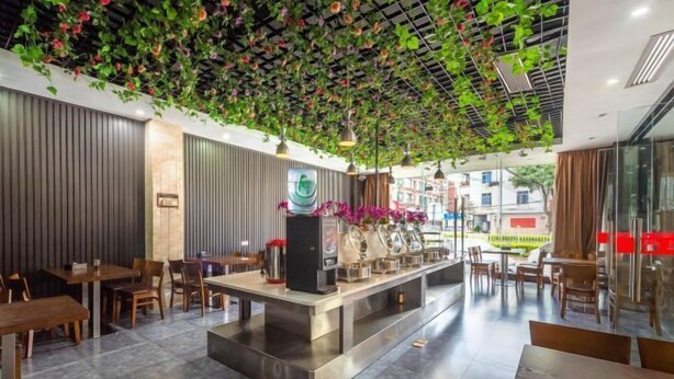 A modern restaurant with a central counter, seating on both sides, and a ceiling adorned with green foliage. - Fuxiang Hotel (Foshan Shunde Lunjiao Branch) (Foshan)