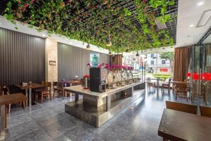 A modern restaurant with a central counter, seating on both sides, and a ceiling adorned with green foliage.
