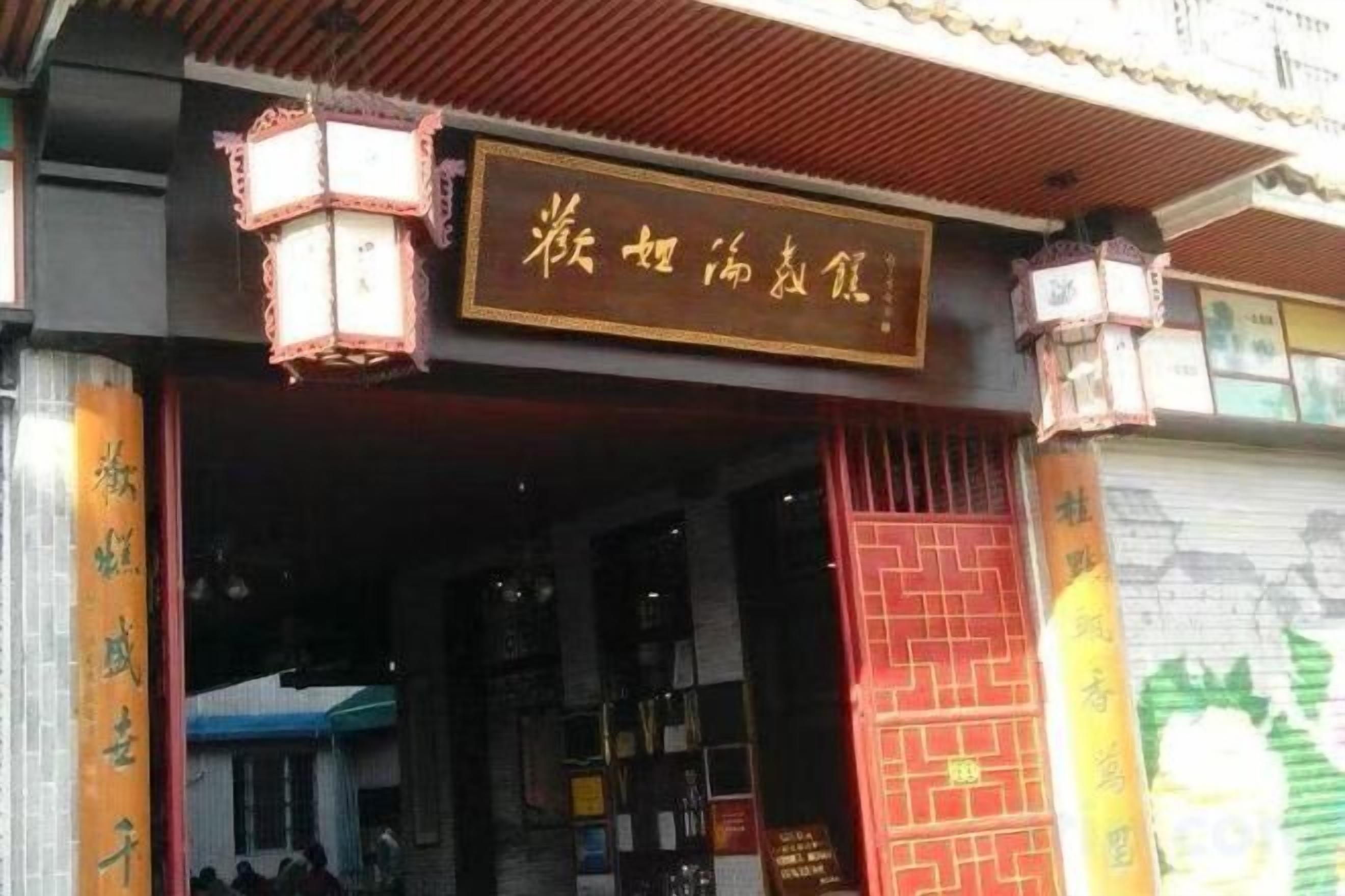 A traditional Chinese building with a signboard, a red gate, and a lantern.