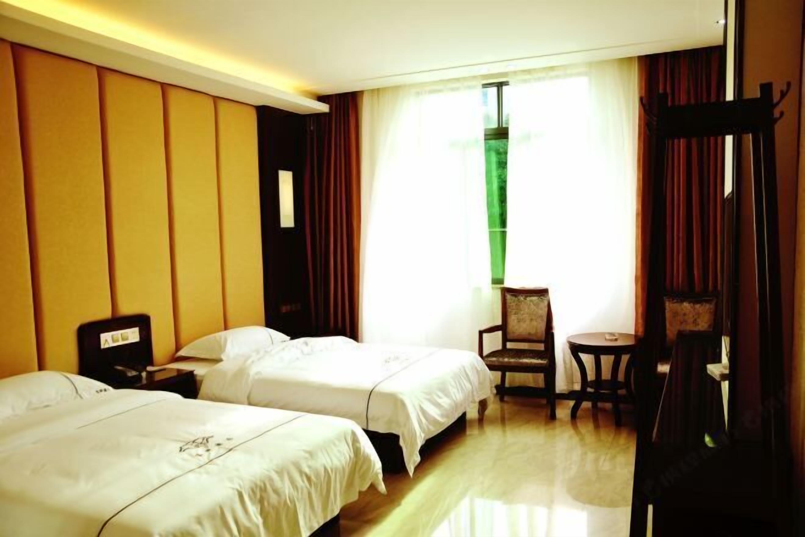 A hotel room with two beds, a small table, a chair, and a window with curtains.