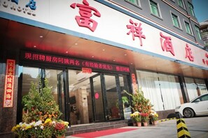Entrada de un hotel con alfombra roja, plantas en macetas y un letrero con caracteres chinos.