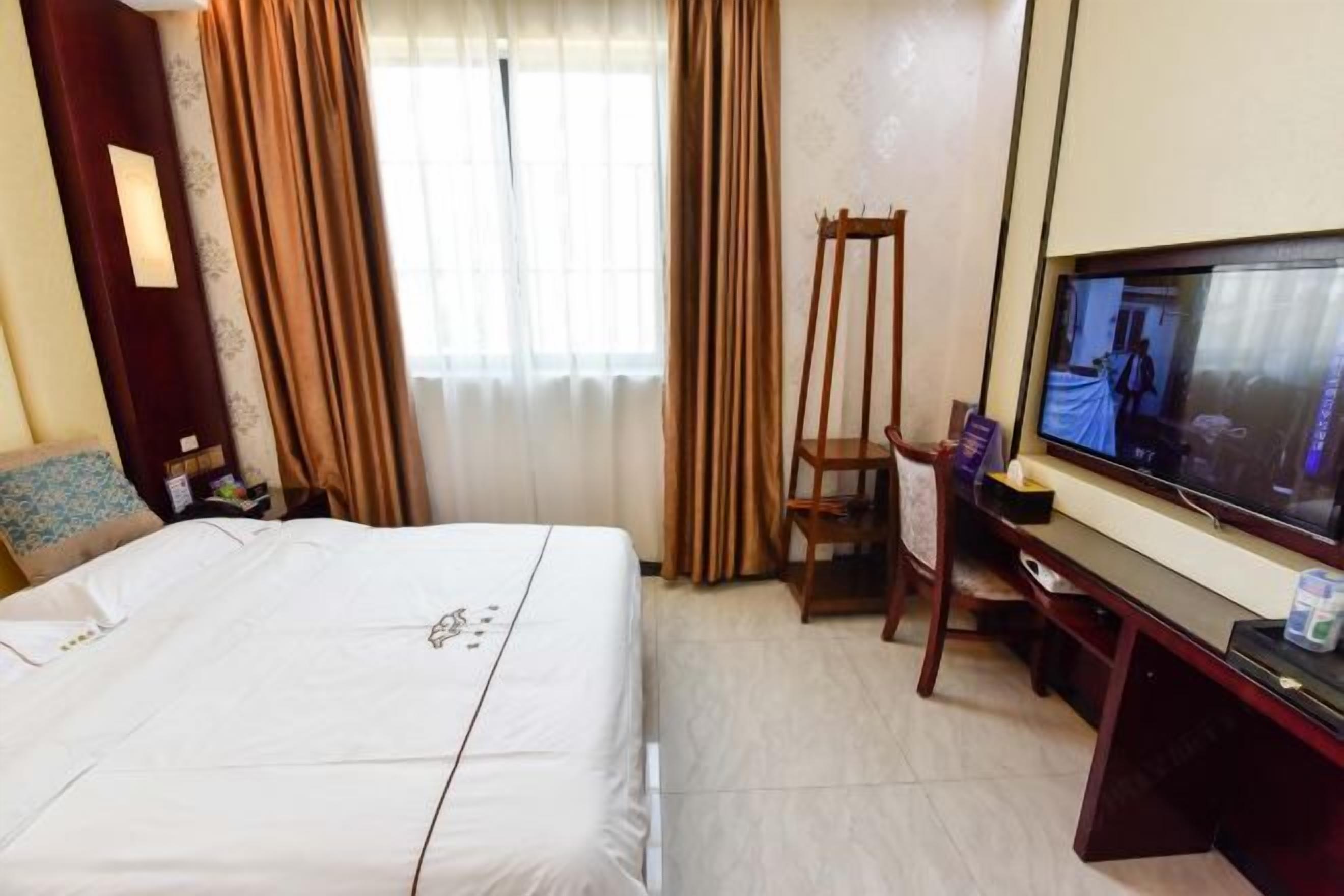 A hotel room with a bed, a desk with a television, a chair, and curtains.