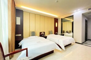 Habitación de hotel con dos camas, una mesita de noche con lámpara, un espejo y vista a un pasillo.