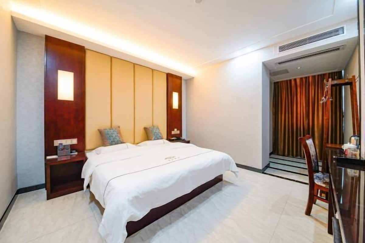 A hotel room with a bed, bedside tables, a chair, a desk, and a curtain.