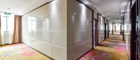 A hotel corridor with a floral carpet, glass partitions, and a long hallway with doors on one side.