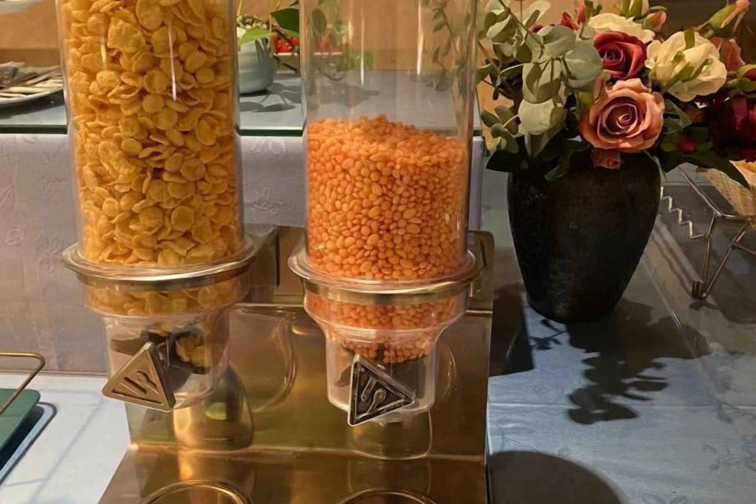 Twee glazen dispensers met snacks, een vaas met bloemen, en een metalen dienblad.