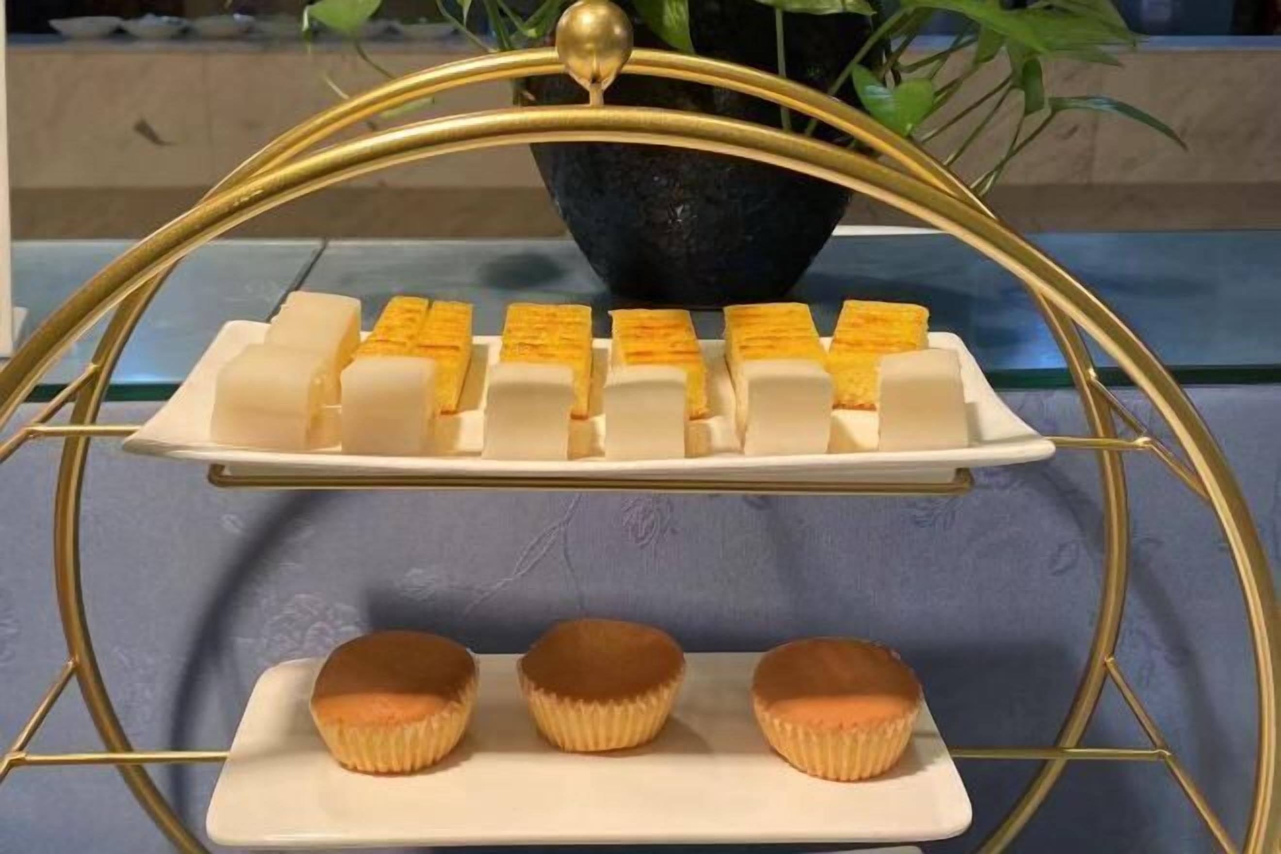 A dessert display with a golden stand, featuring white and yellow rectangular sweets and three cupcakes on a white plate.